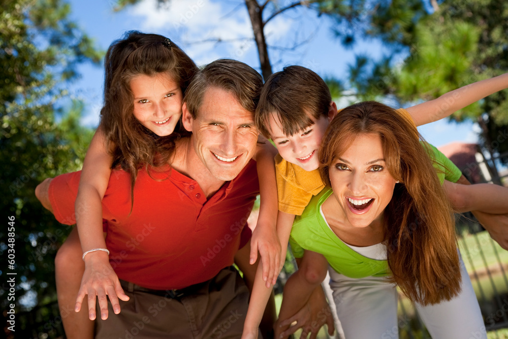 A modern family of father, mother, daughter and son playing together and having doing piggy back in a park A modern family of father, mother, daughter and son playing together and having doing piggy back in a park