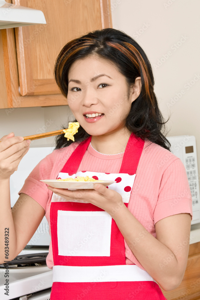 Beautiful Asian woman eating eggs with chop sticks in the kitchen Beautiful Asian woman eating eggs with chop sticks in the kitchen