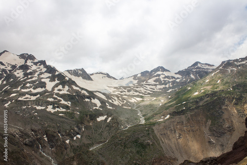 Panoramic landscape - pointed peaks of mountains with white snow and glaciers on the slopes and cloudy sky with dramatic clouds with a blurred horizon in the Elbrus region and copy space