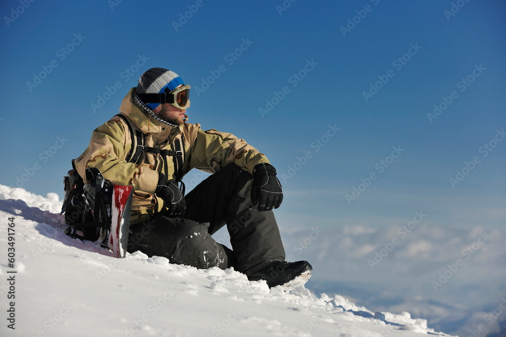 snowboarder relaxing and posing at sunny day on winter season with blue sky in background snowboarder relaxing and posing at sunny day on winter season with blue sky in background