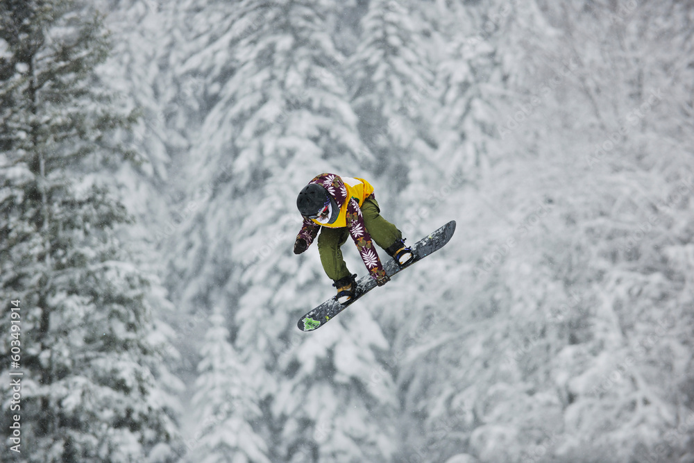 young boys jumping in air ind showing trick with snowboard at winter season