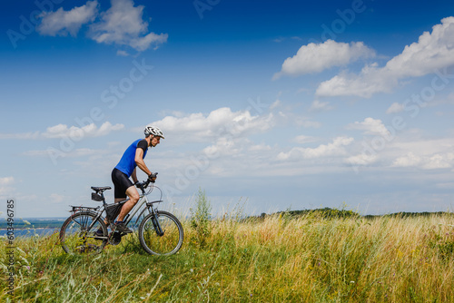 young athletic man on a bicycle riding the green meadow trail on sunny day © olyphotostories