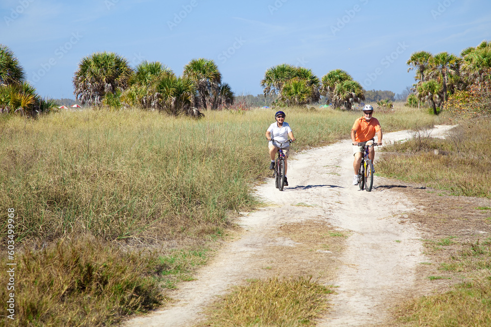Senior couple riding their bikes on a trail beside the beach.