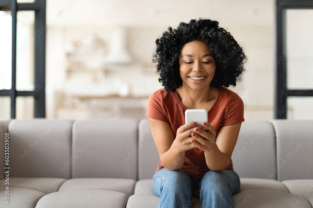 Obraz premium Young Smiling Black Woman With Smartphone Resting On Couch At Home