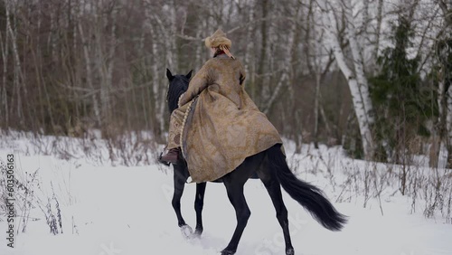 woman riding horse in winter in forest, back view, lady in authentic gown of 12 century, history photo