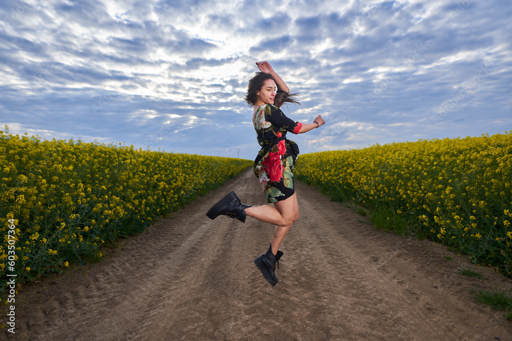 Fototapeta premium Beautiful latino woman in floral dress in a canola field
