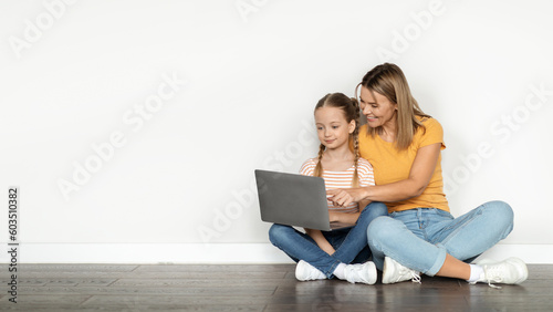 Smiling mother and cute little daughter using laptop together at home