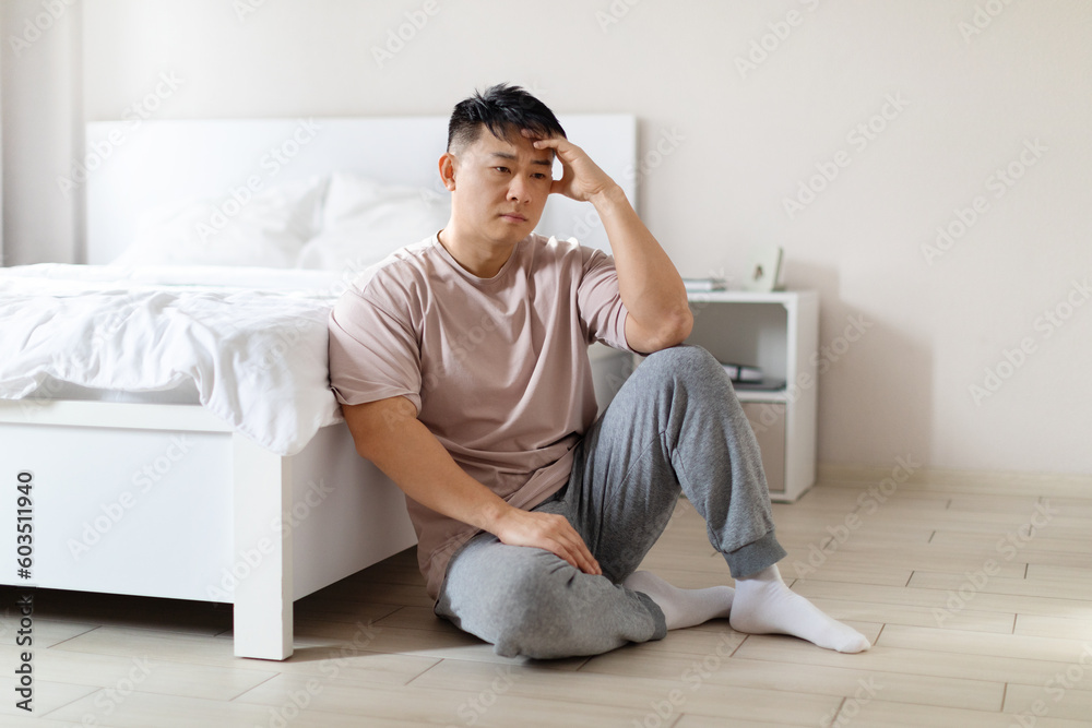 Sad middle aged asian man sitting on bedroom floor