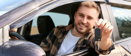Happy young man with key sitting in his new car photo