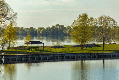 Spring landscape of the river bank with a recreation area and trees on a sunny day