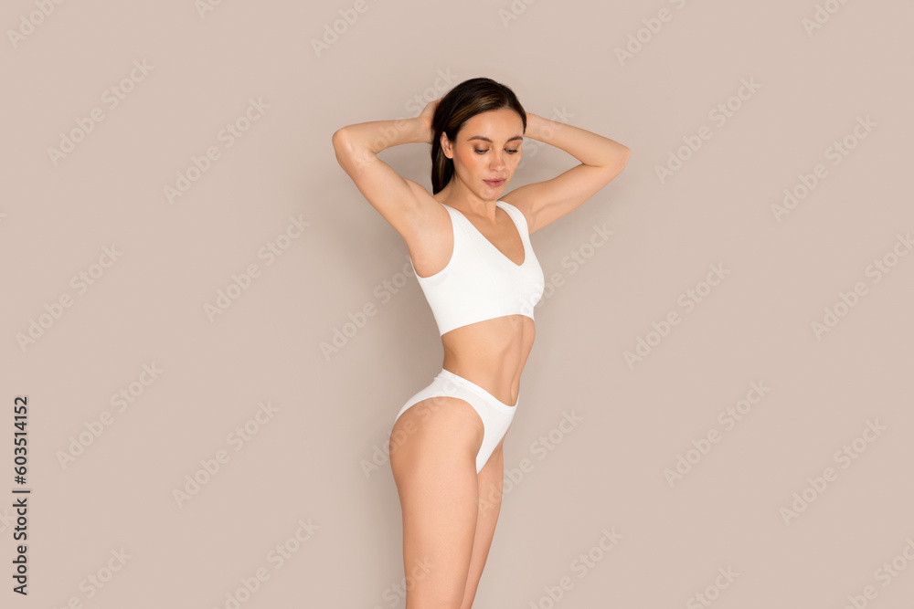 Slim attractive young woman demonstrating perfect body on beige Slim attractive young woman demonstrating perfect body on beige