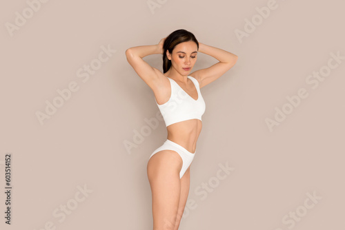 Slim attractive young woman demonstrating perfect body on beige