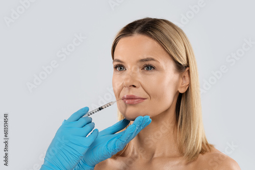 Beautician hands making lips injection for middle aged woman
