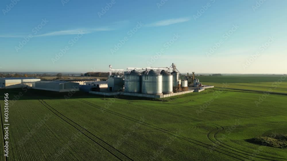 Drone flight over an agricultural field and silver silos at the agro manufacturing plant for processing, drying, cleaning and storage of agricultural products, flour, cereals and legumes. Drone flight over an agricultural field and silver silos at the agro manufacturing plant for processing, drying, cleaning and storage of agricultural products, flour, cereals and legumes.