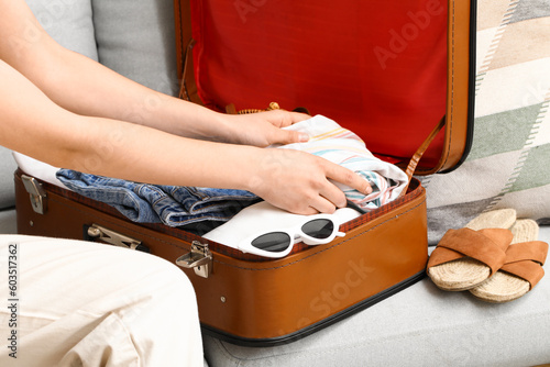 Woman packing clothes into suitcase on sofa at home, closeup