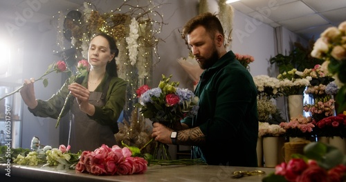 Two florists entrepreneurs together create beautiful multicolor bouquet in flower shop. Woman helps colleague and adds fresh flowers to bunch. Concept of retail floral business and entrepreneurship.