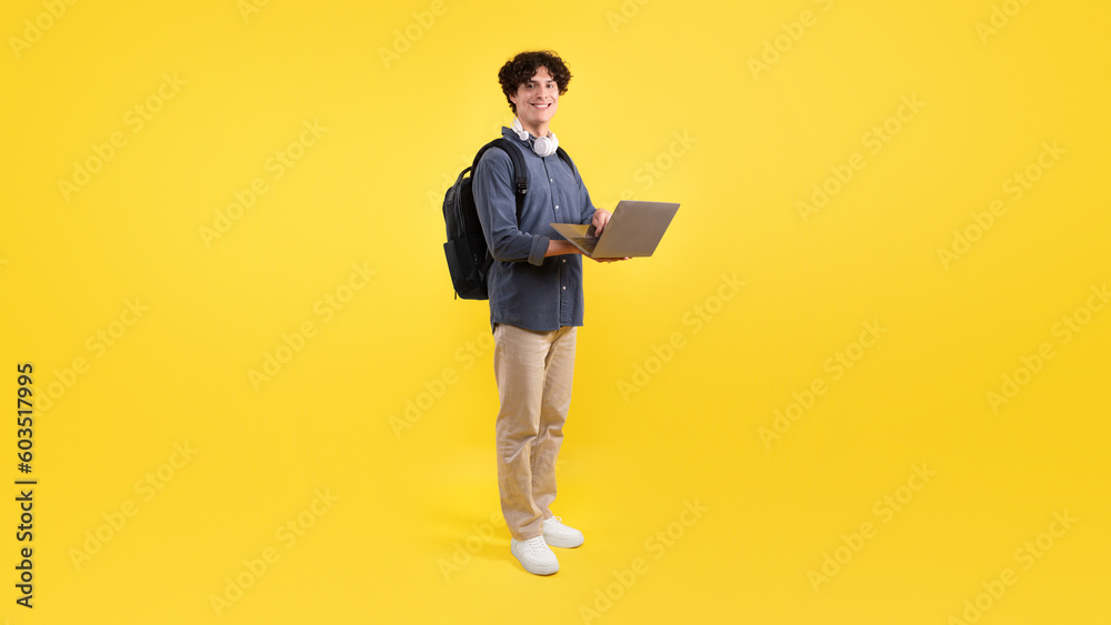 Student Guy Using Laptop Standing With Backpack Over Yellow Background Student Guy Using Laptop Standing With Backpack Over Yellow Background