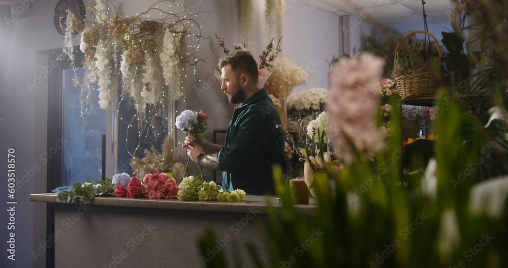Professional florist adds branches to flowers in floral shop. Male entrepreneur collects beautiful bouquet. Buyer or coworker walks with bouquet. Retail floral business and entrepreneurship concept.