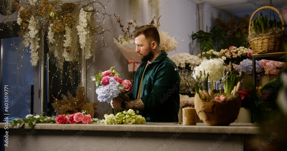Professional florist adds branches to flowers in floral shop. Male entrepreneur collects beautiful bouquet. Buyer or coworker walks with bouquet. Retail floral business and entrepreneurship concept.