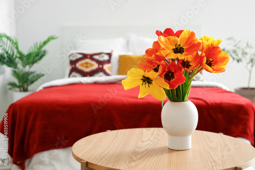 Vase with beautiful tulip flowers on wooden table in interior of bedroom