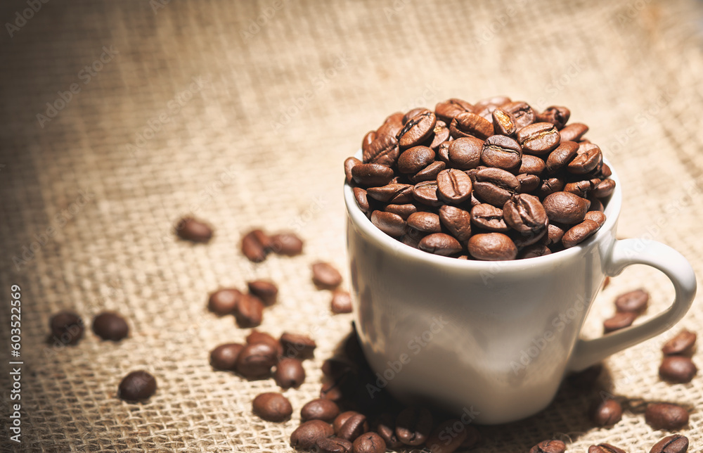Fototapeta premium Cup full of coffee beans on sisal fabric