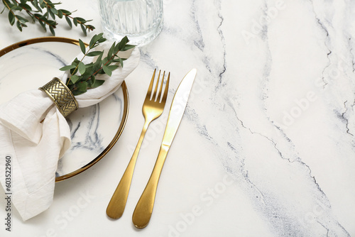 Plate with folded napkin and gold cutlery on grunge white background