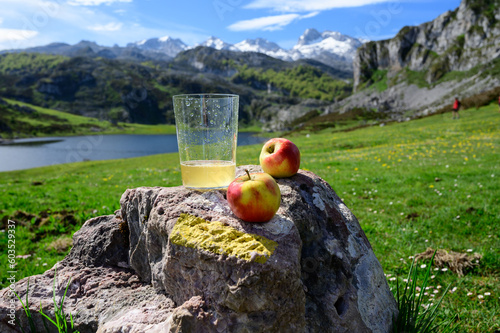 Fototapeta Naklejka Na Ścianę i Meble -  Glass of natural Asturian cider made from fermented apples with view on Covadonga lake and tops of Picos de Europa mountains, Spain