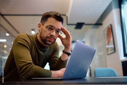 Worried businessman reading problematic email on laptop in office. photo