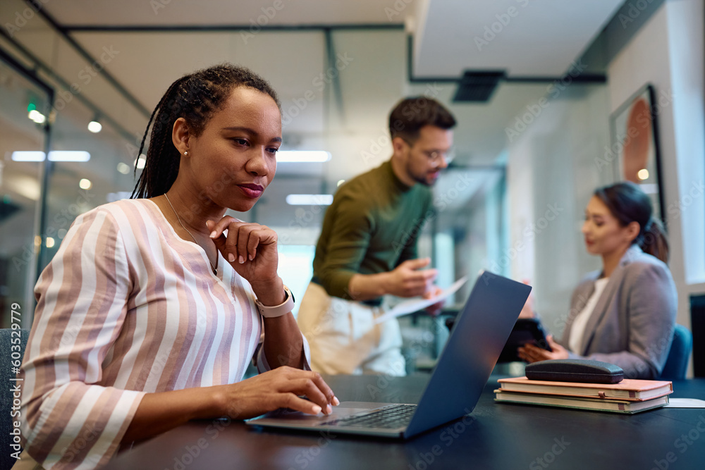 Black female entrepreneur working on laptop in office.