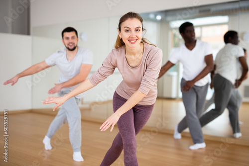 Caucasian woman dancing aerobic dance with men in studio during group training.