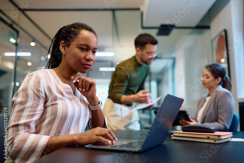 Black female entrepreneur working on laptop in office.