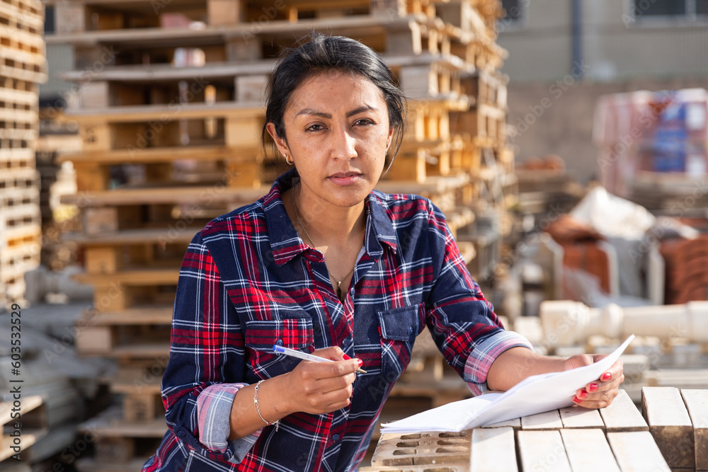 Obraz premium Latin American female supervisor checking quality of redbricks at hardware store warehouse