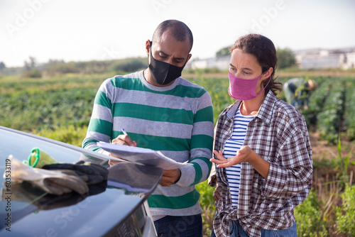 Courier in protective mask invites the farmer to sign documents on the farmer field © JackF