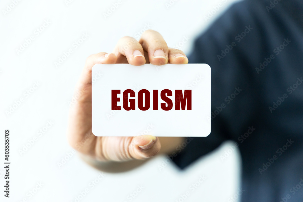 Egoism text on blank business card being held by a woman's hand with blurred background. Business concept about egoism. Egoism text on blank business card being held by a woman's hand with blurred background. Business concept about egoism.