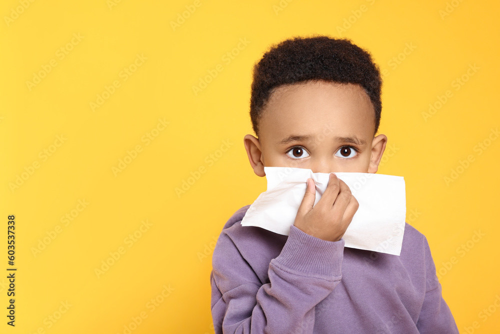 African-American boy blowing nose in tissue on yellow background, space for text. Cold symptoms African-American boy blowing nose in tissue on yellow background, space for text. Cold symptoms
