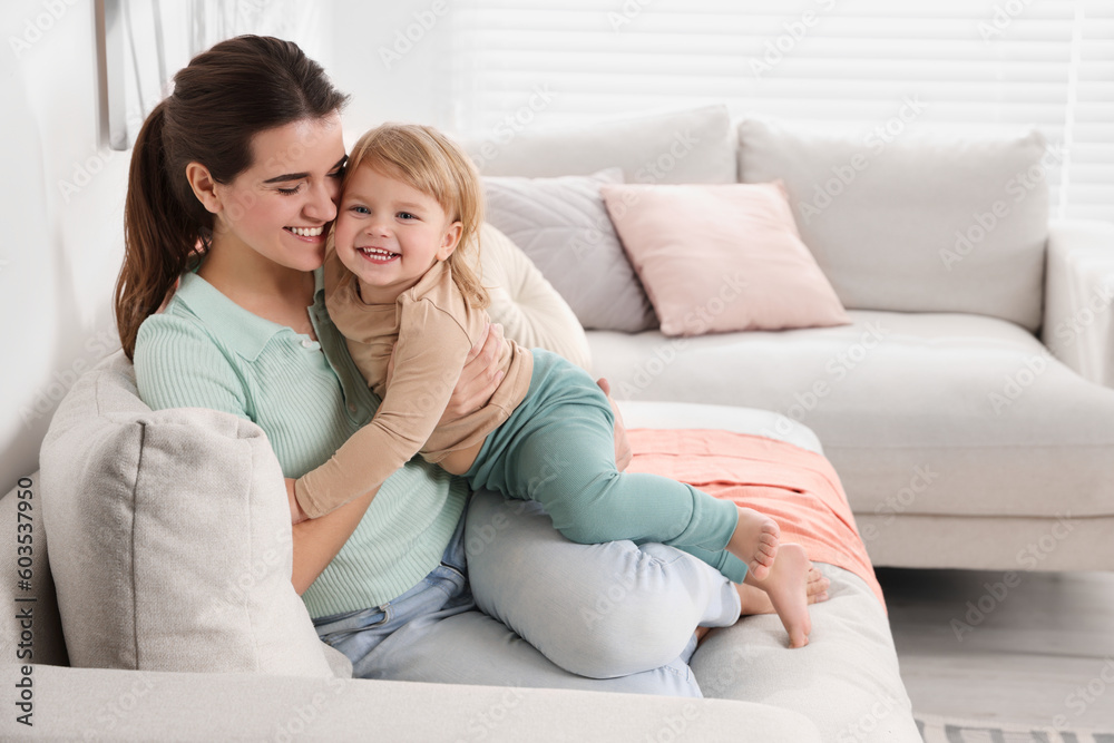Mother with her cute little daughter on sofa at home, space for text