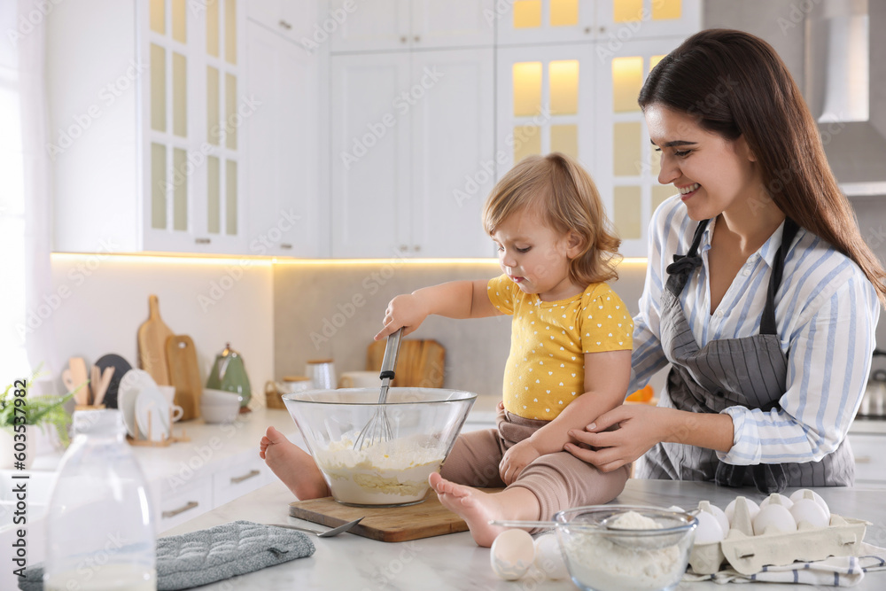 Mother and her little daughter cooking dough together in kitchen Mother and her little daughter cooking dough together in kitchen