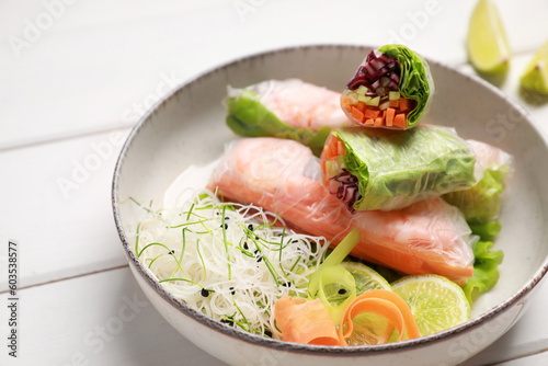 Delicious spring rolls wrapped in rice paper on white wooden table, closeup