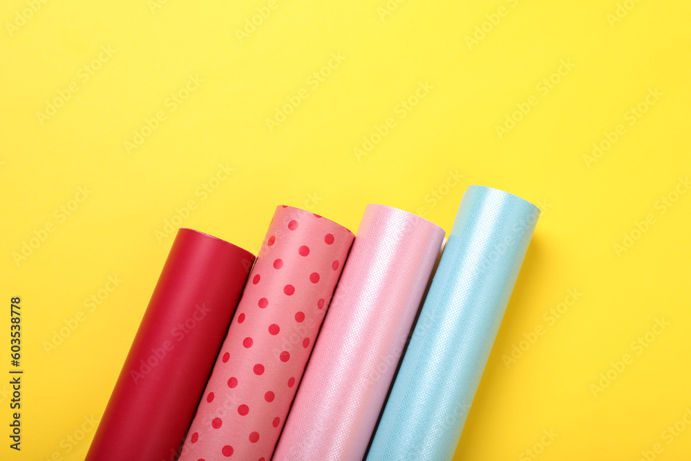Rolls of colorful wrapping papers on yellow background, flat lay. Space for text