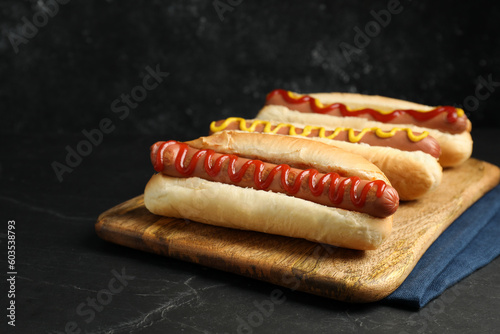 Fresh delicious hot dogs with sauces on black table