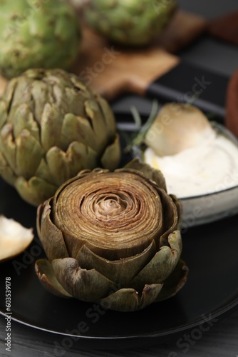 Delicious cooked artichokes with tasty sauce on plate, closeup