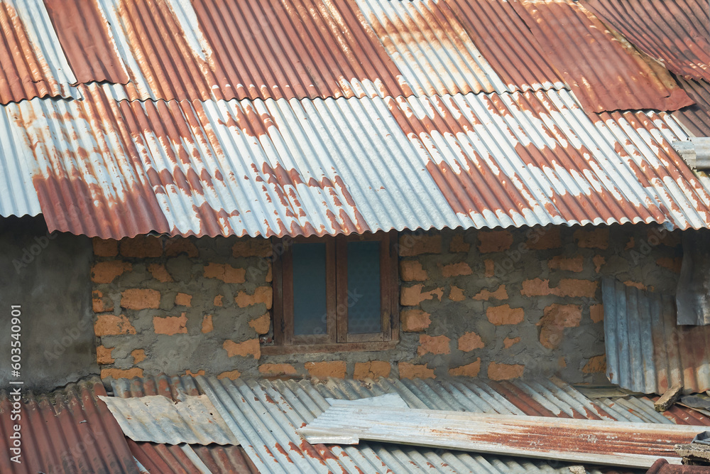 close-up view of old damaged village shanty house, temporary building made of unbaked brick wall with cement and rusty metal corrugated roofing sheets in remote areas, copy space close-up view of old damaged village shanty house, temporary building made of unbaked brick wall with cement and rusty metal corrugated roofing sheets in remote areas, copy space