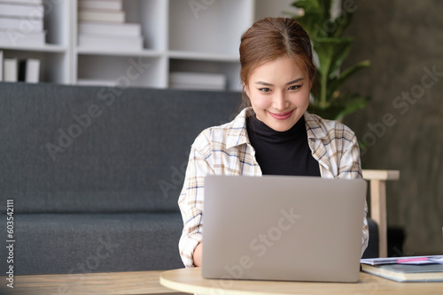 Attractive young woman freelancer sitting at desk in living room and working on laptop.