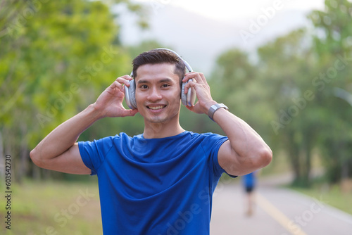 Athletic young man in sport wears listening to music in headphone while taking break after morning training in the plubric park.