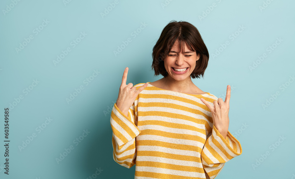 Joyful ethnic lady showing horns sign and smiling in blue studio Joyful ethnic lady showing horns sign and smiling in blue studio