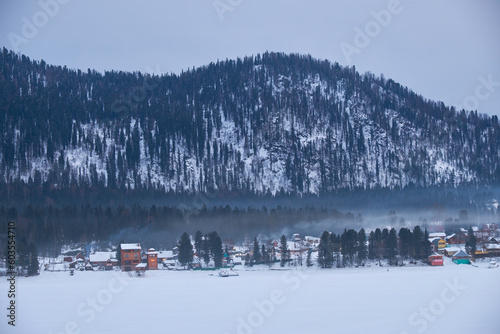 Houses on the bank of frozen Teletskoe lake under the chimney smoke. Iogach, Altai. photo