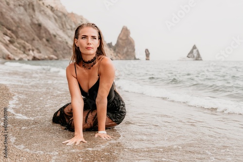 Woman summer travel sea. Happy tourist in black dress enjoy taking picture outdoors for memories. Woman traveler posing on sea beach surrounded by volcanic mountains, sharing travel adventure journey