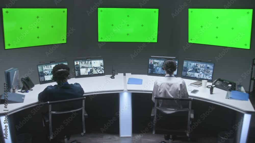 Multi ethnic male and female officers control CCTV cameras. Employees work in security control center. Computer monitors showing surveillance cameras video footage. Big digital screens with chromakey.
