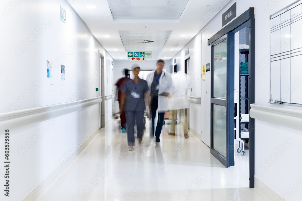 Blurred motion of diverse doctors and medical staff in busy hospital corridor, copy space