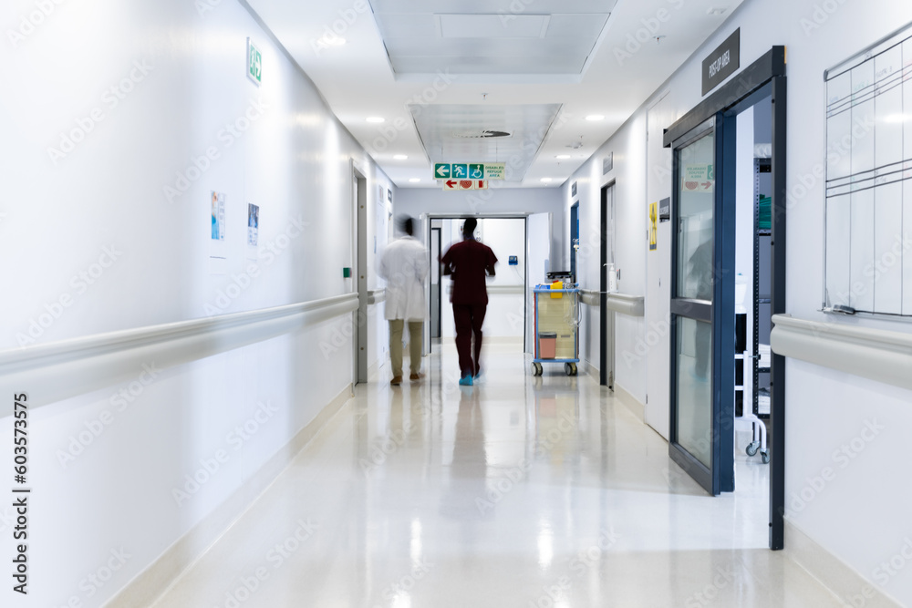 Blurred motion of diverse doctors walking in busy hospital corridor, copy space